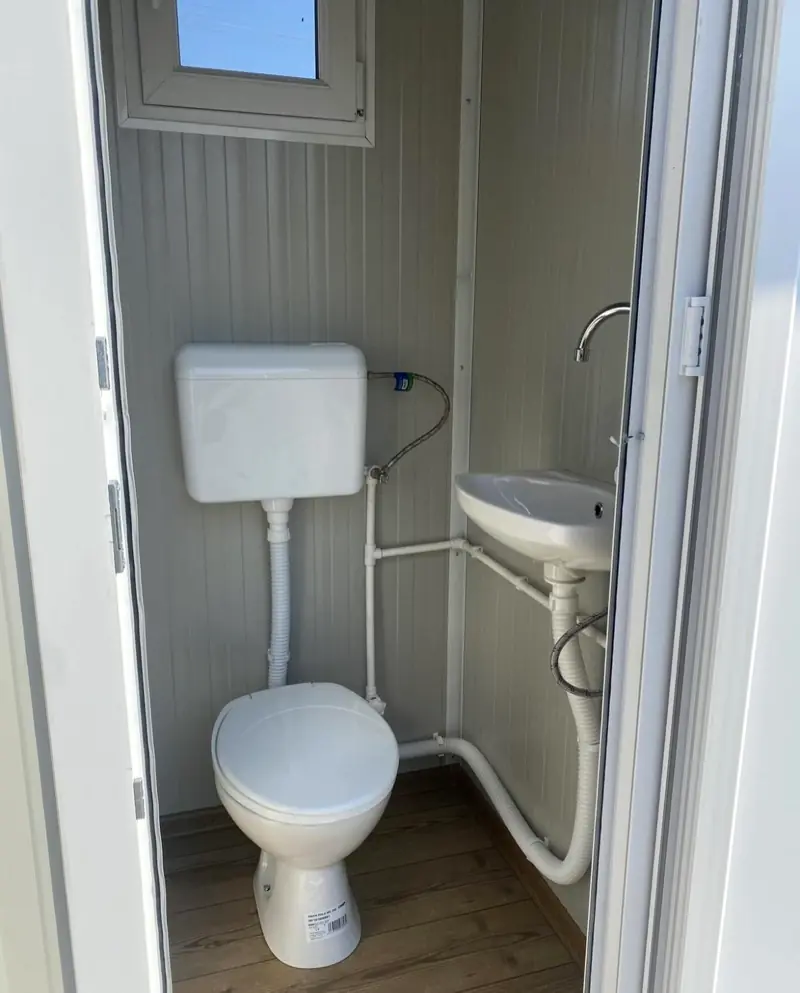 Flushing tank toilet and small wall sink inside a restroom cabin