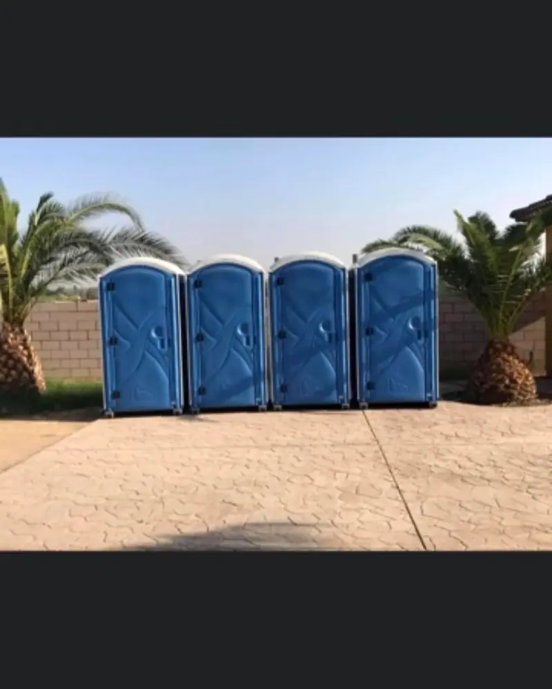 Four blue standard porta potties lined up on a paved pad