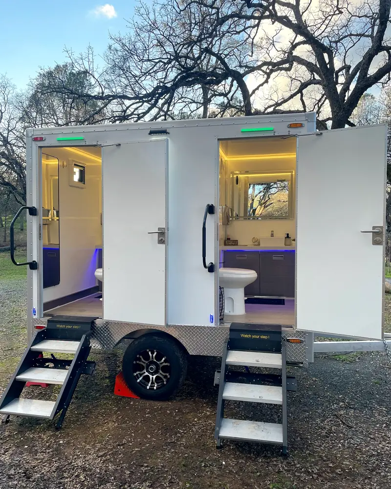Luxury restroom trailer with both stall doors open and interior lights on
