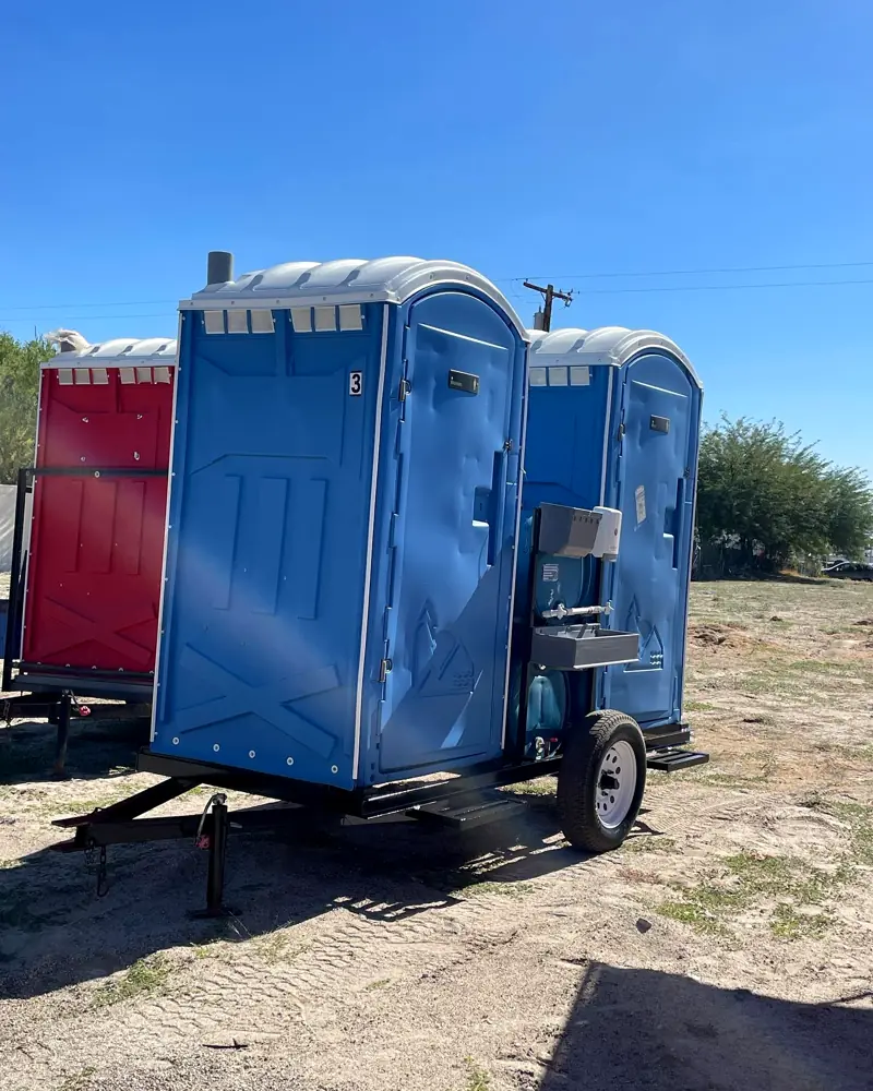 Blue porta potties and a sink strapped on a transport trailer