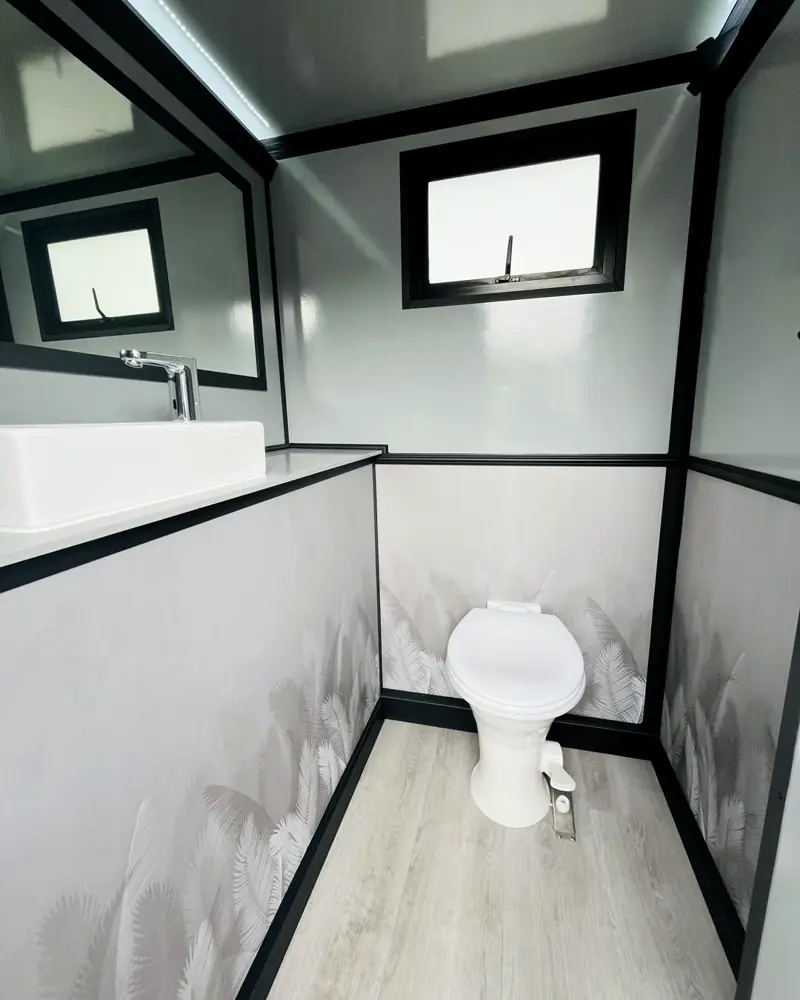 Inside a restroom trailer stall with a flushing toilet, vanity sink and window