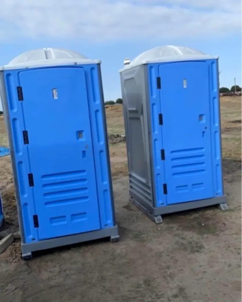 Two blue standard porta potties on open dirt under a clear sky