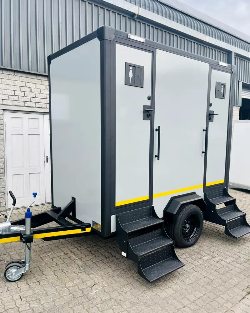 Two-station restroom trailer with separate doors and fold-down steps on a brick lot